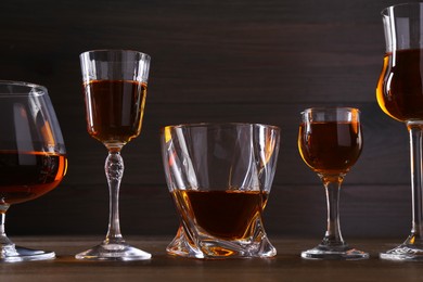 Photo of Different delicious liqueurs in glasses on wooden table