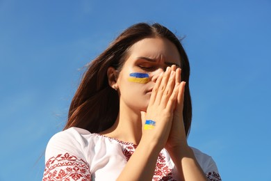 Photo of Young Ukrainian woman with clasped hands against blue sky