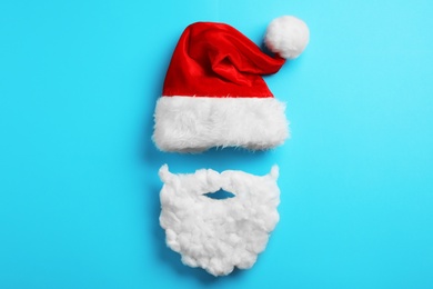 Photo of Santa Claus hat and beard on light blue background, flat lay