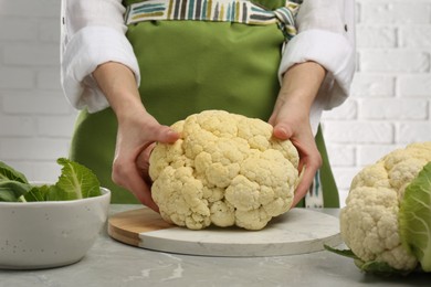 Woman with fresh cauliflower at light grey table, closeup