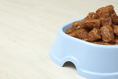 Wet pet food in feeding bowl on white table, closeup. Space for text