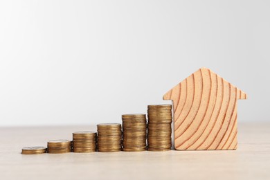 Mortgage concept. House model and stacks of coins on wooden table against white background, space for text