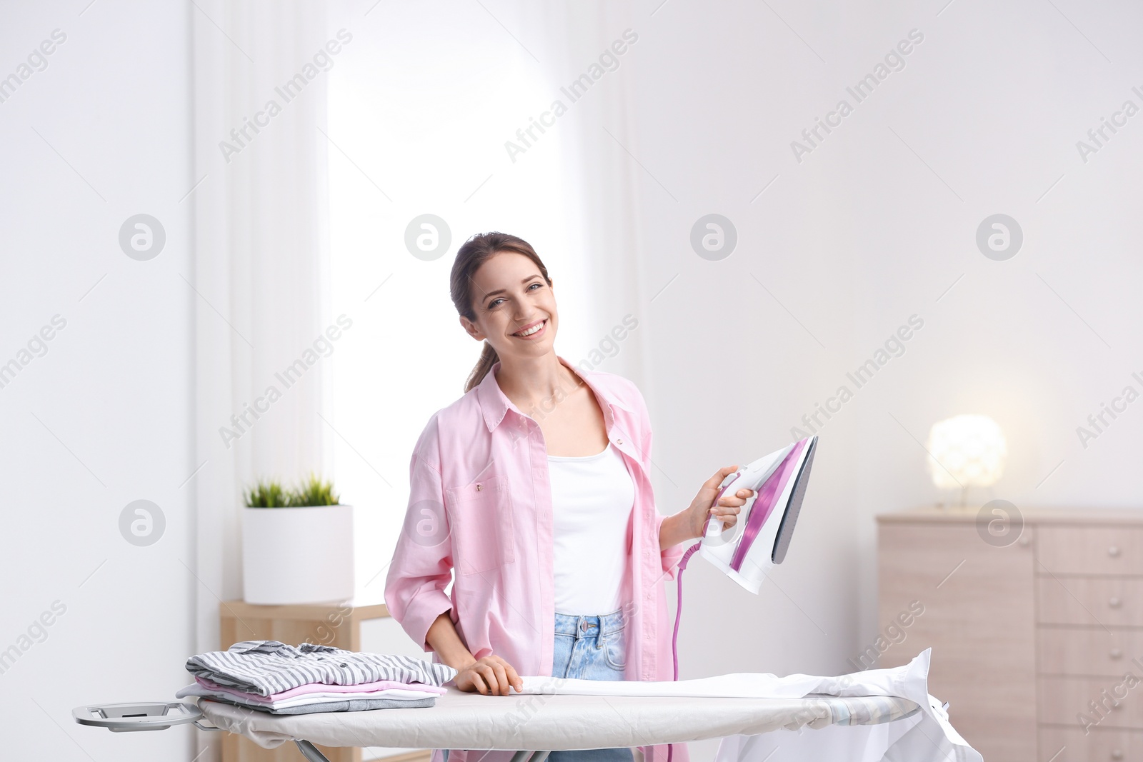 Photo of Young pretty woman ironing clean laundry indoors