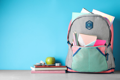 Stylish backpack with different school stationery on table against light blue background. Space for text