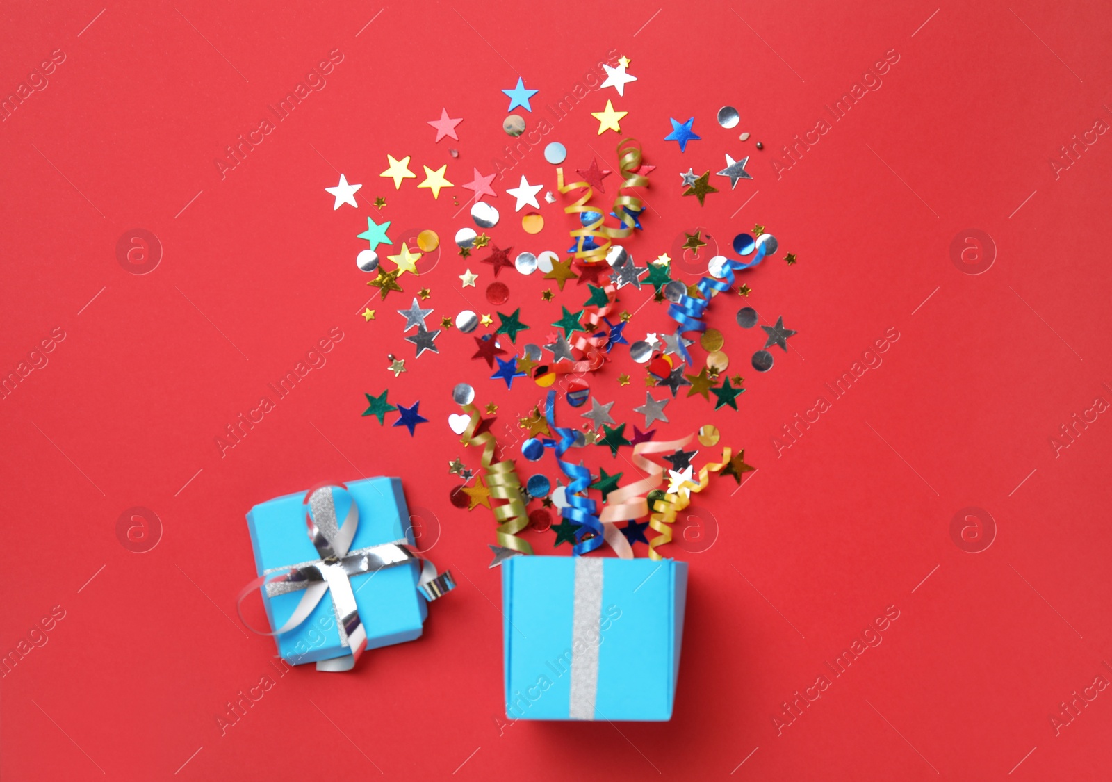 Photo of Box with bright confetti on red background, flat lay