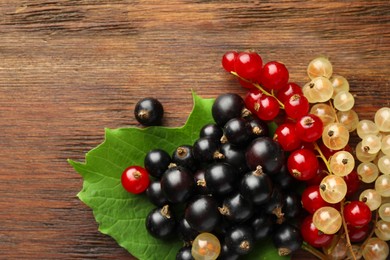 Photo of Different fresh ripe currants and green leaf on wooden table, top view