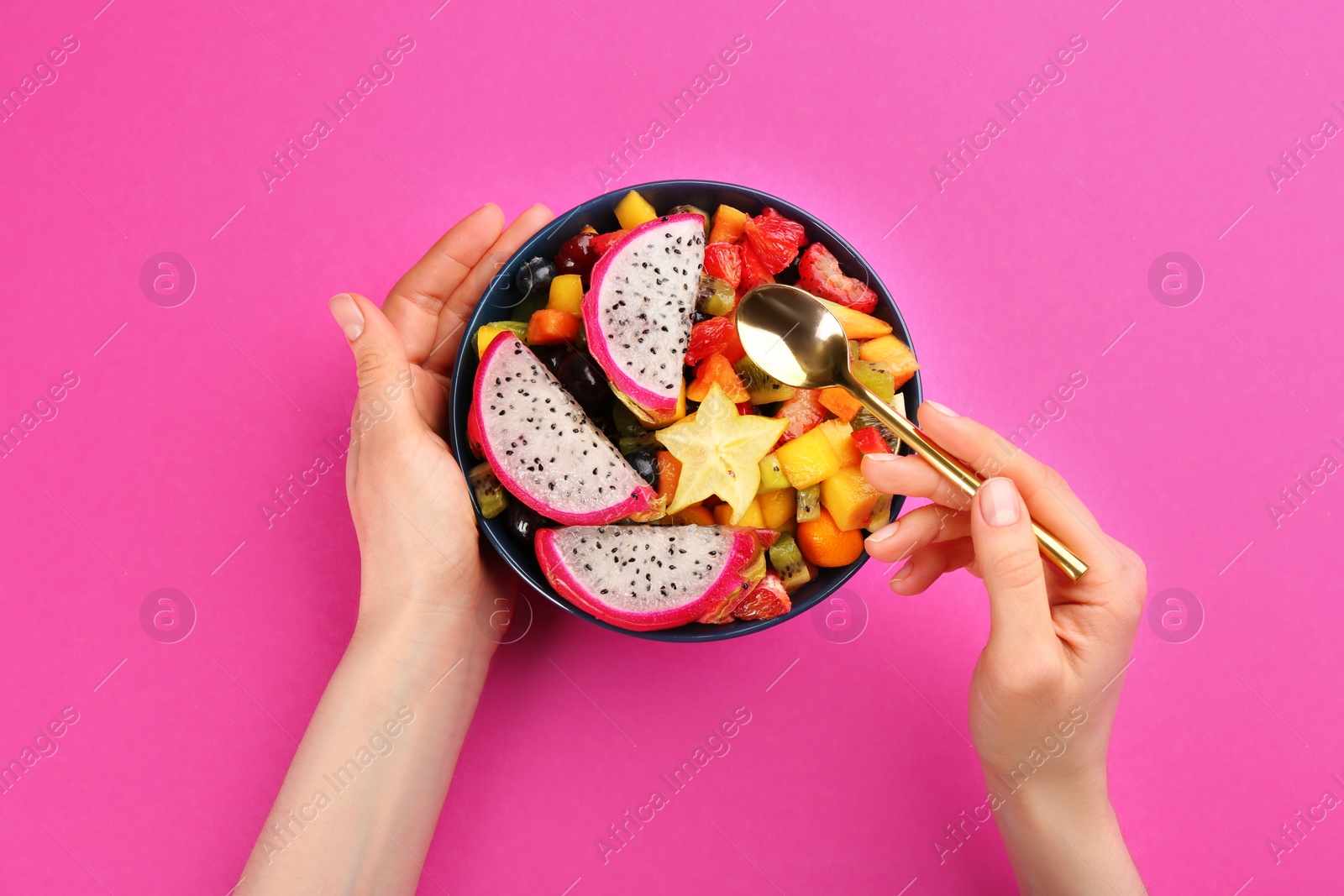 Photo of Woman with bowl of delicious exotic fruit salad on pink background, top view