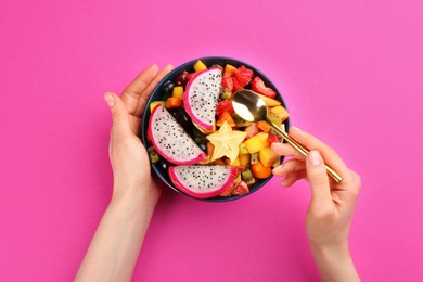 Photo of Woman with bowl of delicious exotic fruit salad on pink background, top view