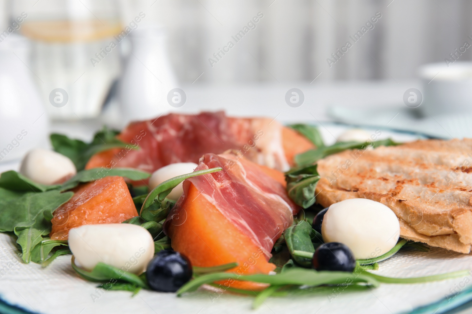 Photo of Fresh melon with prosciutto, mozzarella and arugula on plate, closeup