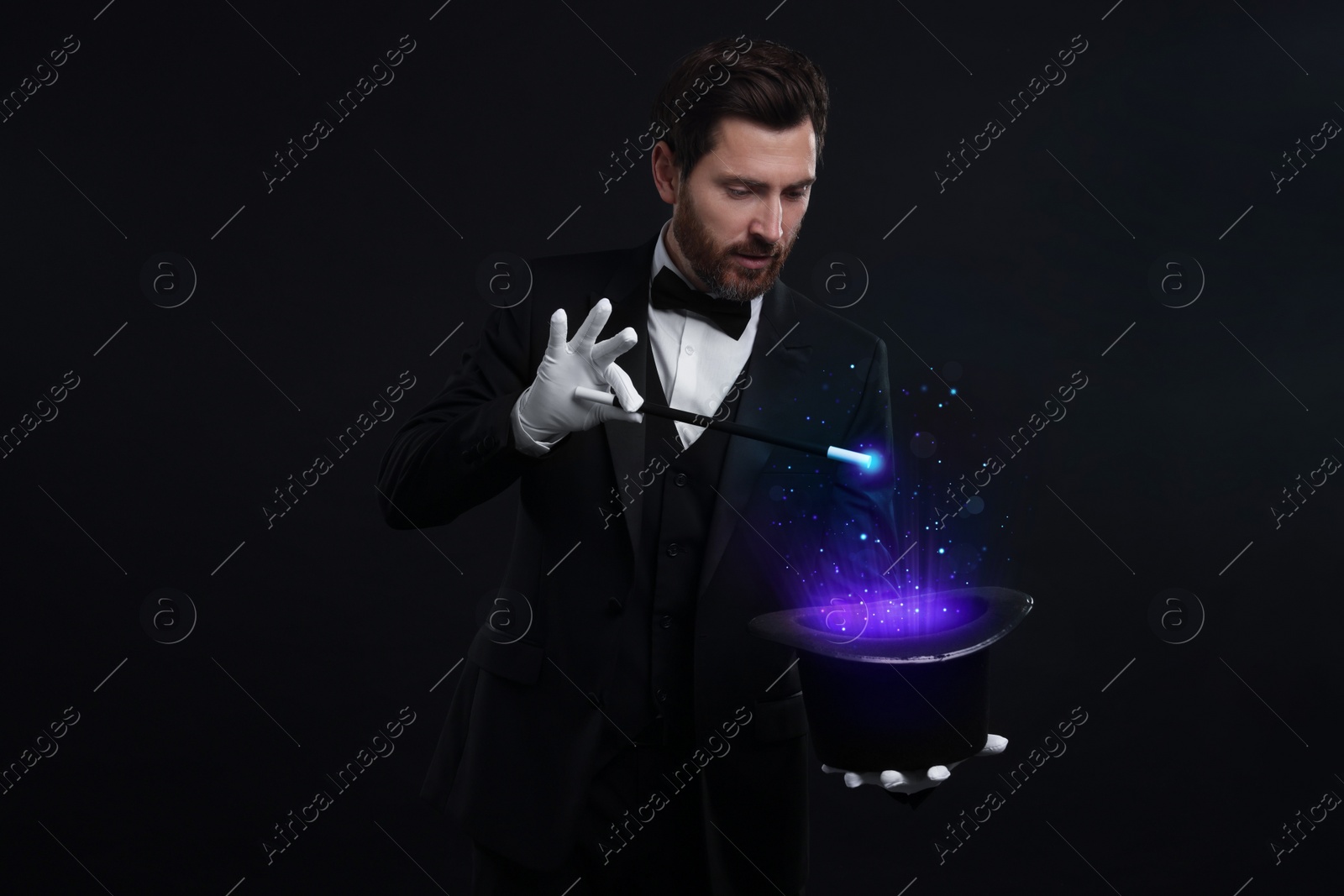 Image of Magician showing trick with top hat and wand on black background