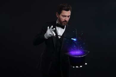 Magician showing trick with top hat and wand on black background