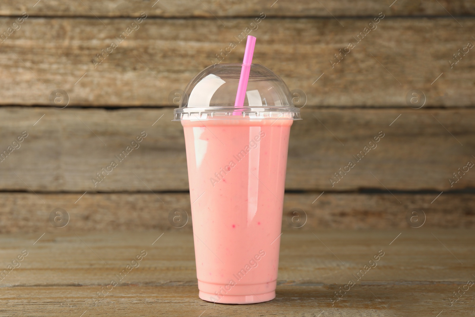 Photo of Plastic cup of tasty smoothie on wooden table