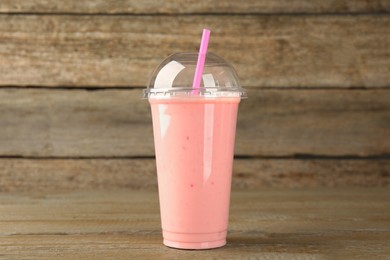 Photo of Plastic cup of tasty smoothie on wooden table