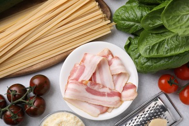 Photo of Raw pasta, bacon and fresh ingredients on light grey table, flat lay