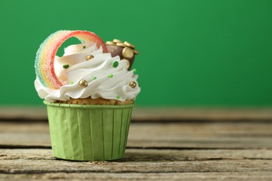 Photo of St. Patrick's day party. Tasty cupcake with sour rainbow belt and pot of gold toppers on wooden table, closeup. Space for text