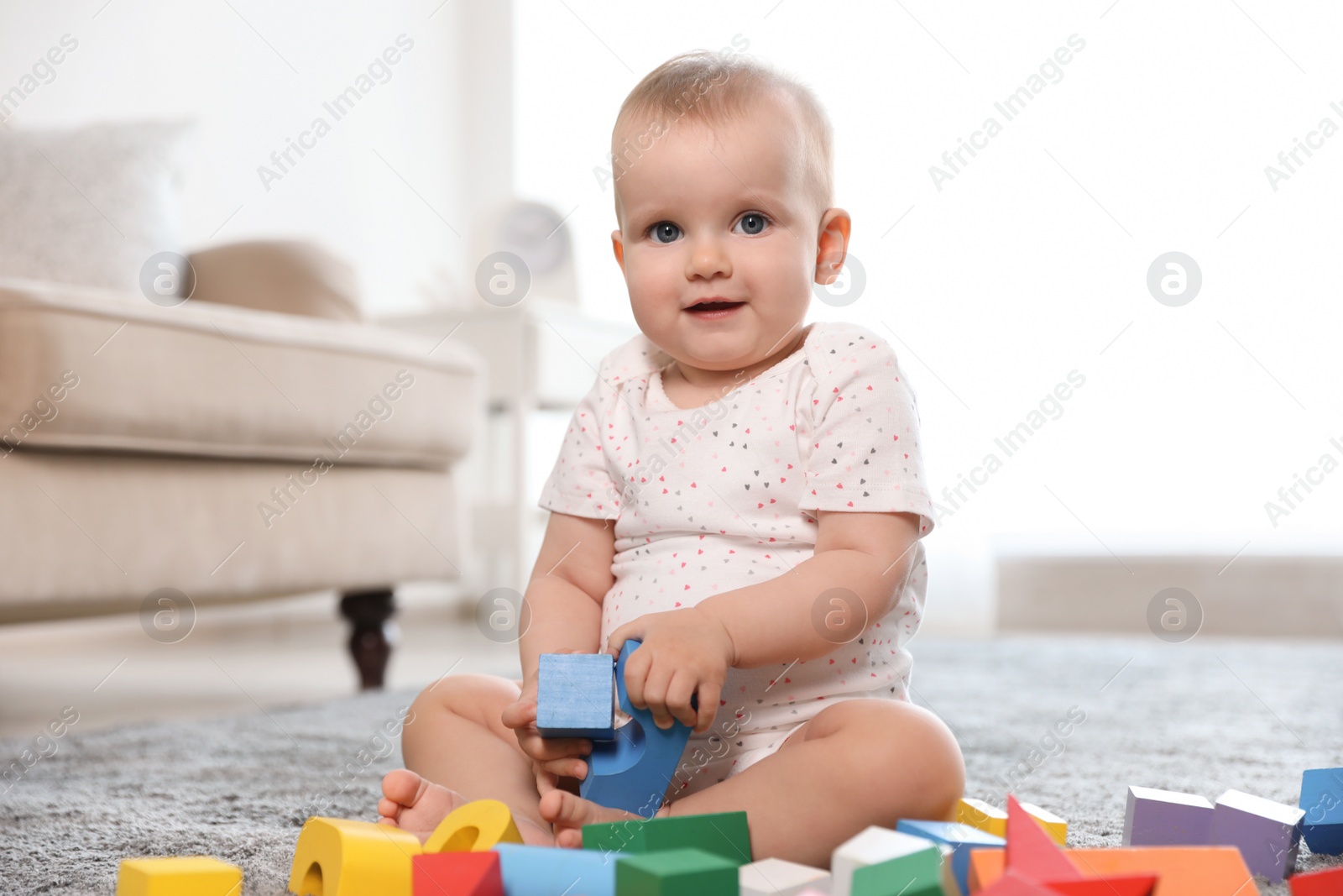 Photo of Cute baby girl playing with building blocks in room