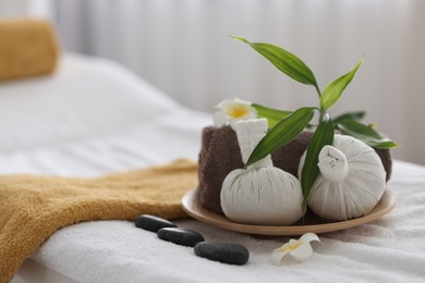 Photo of Spa stones, flowers, towel and herbal bags on massage table indoors