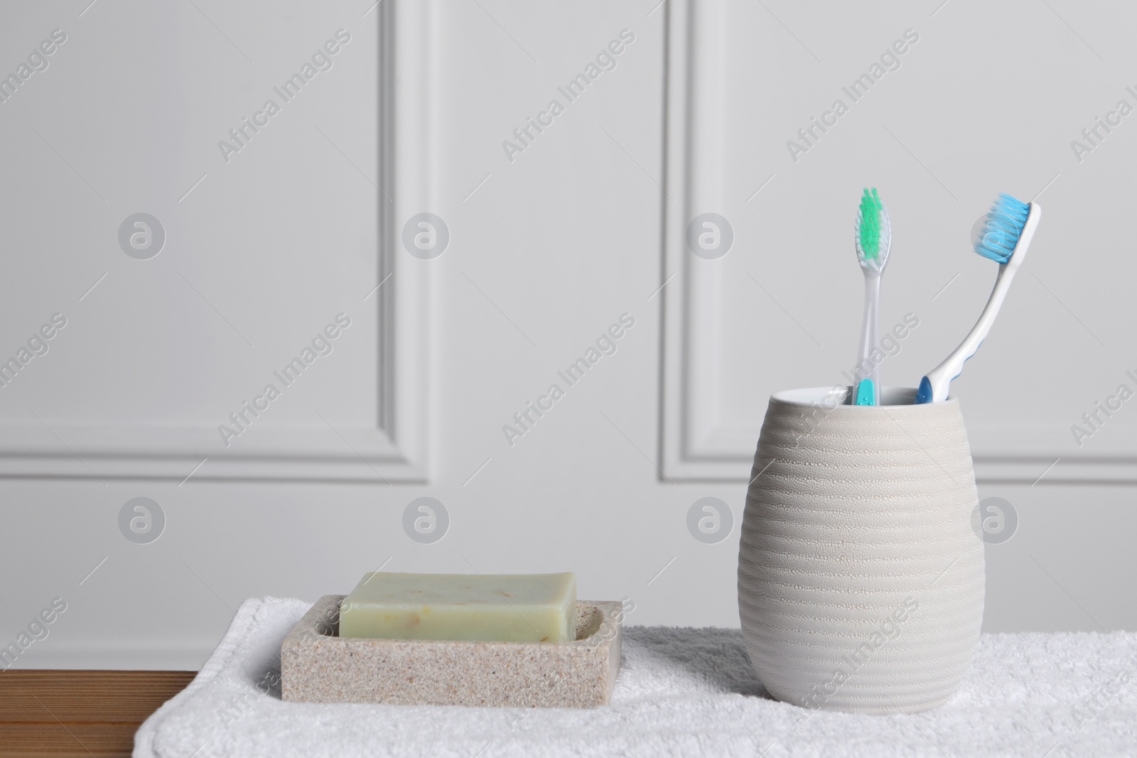 Photo of Plastic toothbrushes in holder, towel and soap bars on wooden table. Space for text