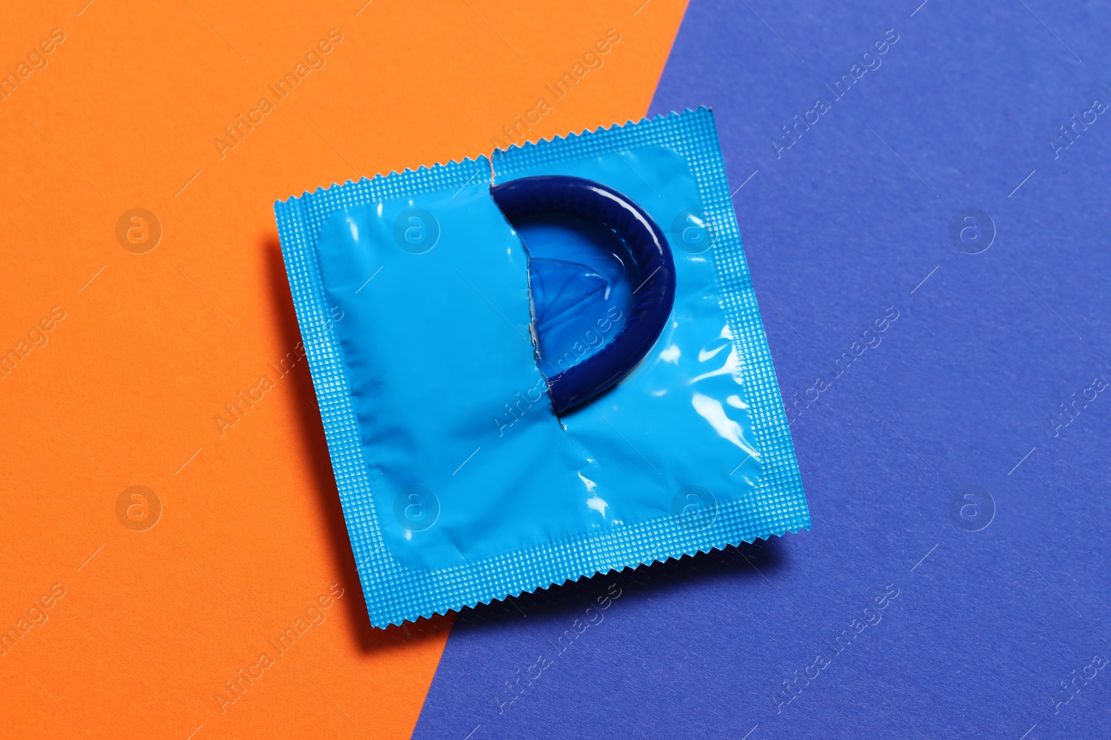 Photo of Condom in torn package on color background, top view. Safe sex