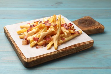 Photo of Delicious French fries with bacon and cheese sauce on light blue wooden table