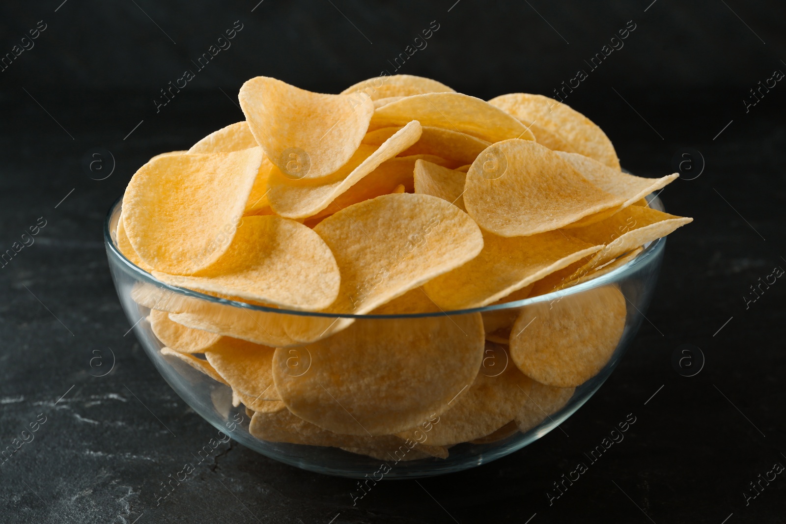 Photo of Bowl with delicious potato chips on black table, closeup