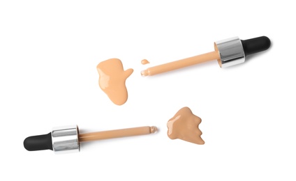 Samples of different foundation shades and droppers on white background, top view