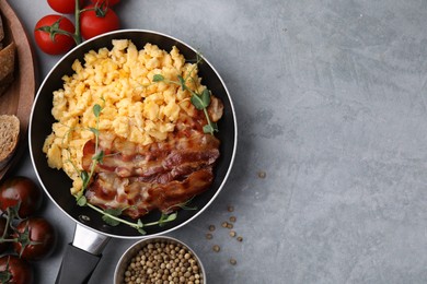 Photo of Delicious scrambled eggs with bacon in frying pan and ingredients on grey table, flat lay. Space for text