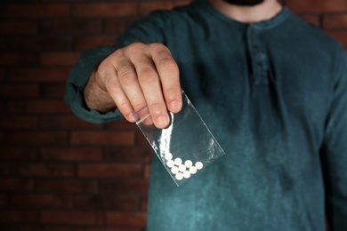 Photo of Male dealer holding drugs in plastic bag near brick wall, closeup