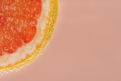 Photo of Slice of grapefruit in sparkling water on light pink background, closeup with space for text. Citrus soda