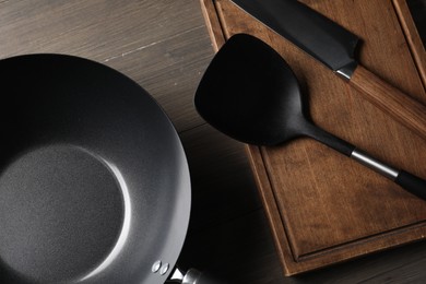 Black metal wok, knife, board and spatula on wooden table, top view