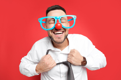 Photo of Joyful man with funny glasses on red background. April fool's day
