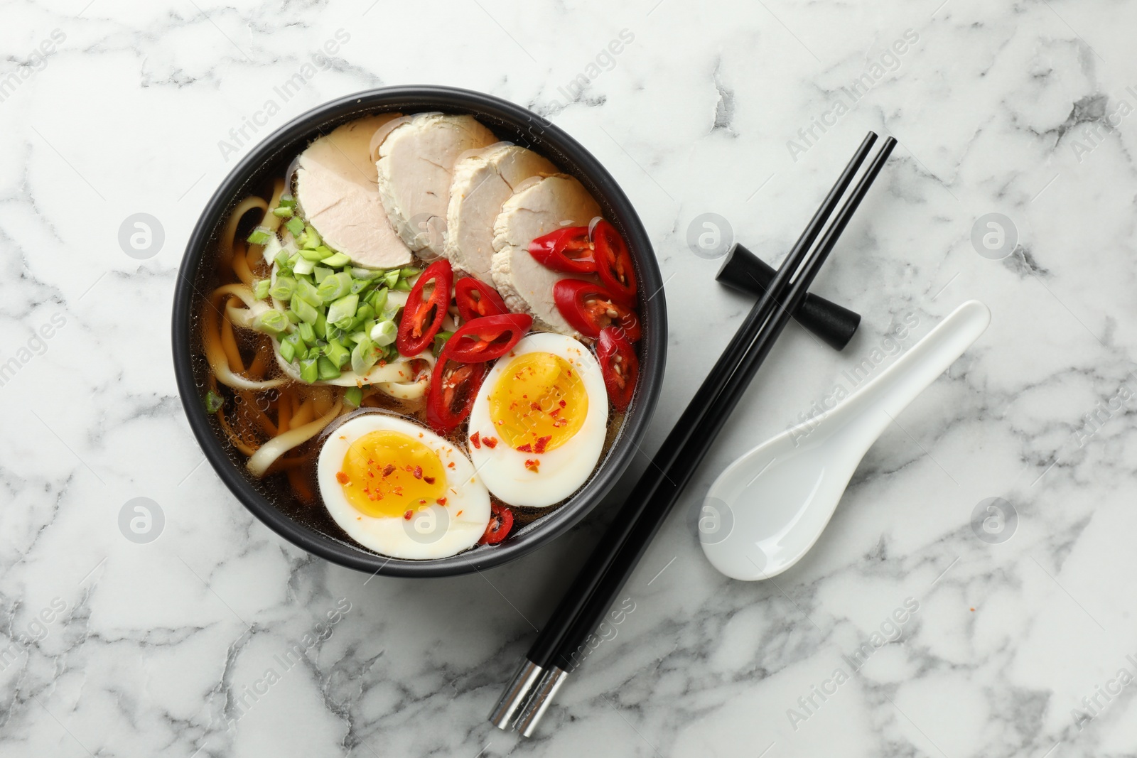 Photo of Delicious ramen in bowl and spoon on white marble table, flat lay. Noodle soup