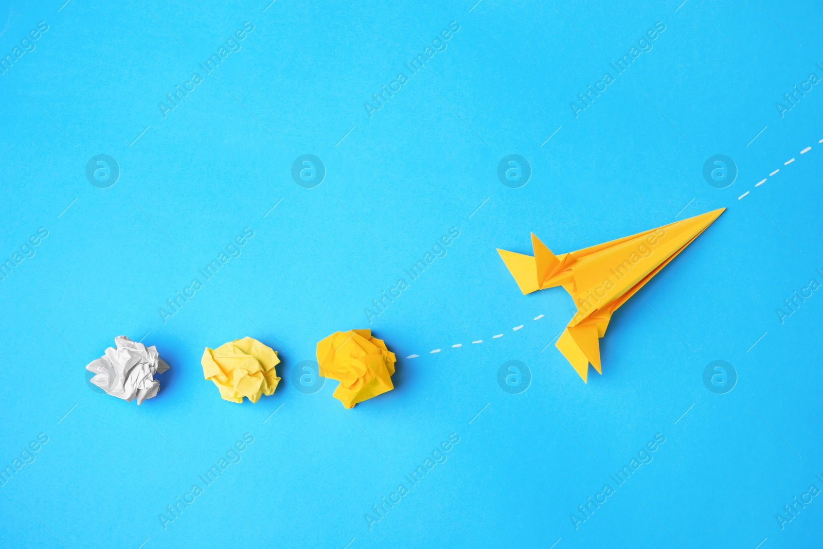 Photo of Handmade orange rocket and crumpled pieces of paper on light blue background, flat lay with space for text