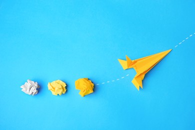 Handmade orange rocket and crumpled pieces of paper on light blue background, flat lay with space for text