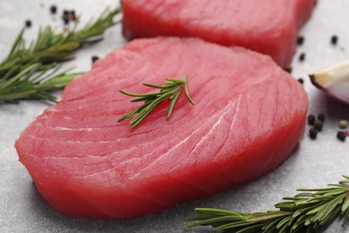 Photo of Fresh raw tuna fillet and rosemary on light gray table, closeup