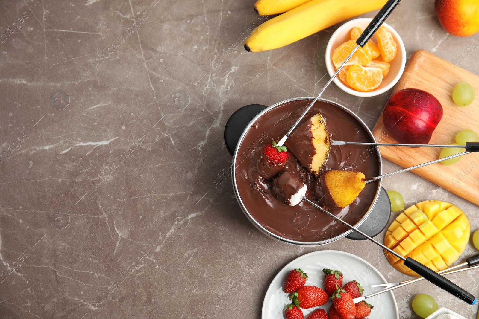 Photo of Flat lay composition with chocolate fondue in pot, fruits and space for text on gray background