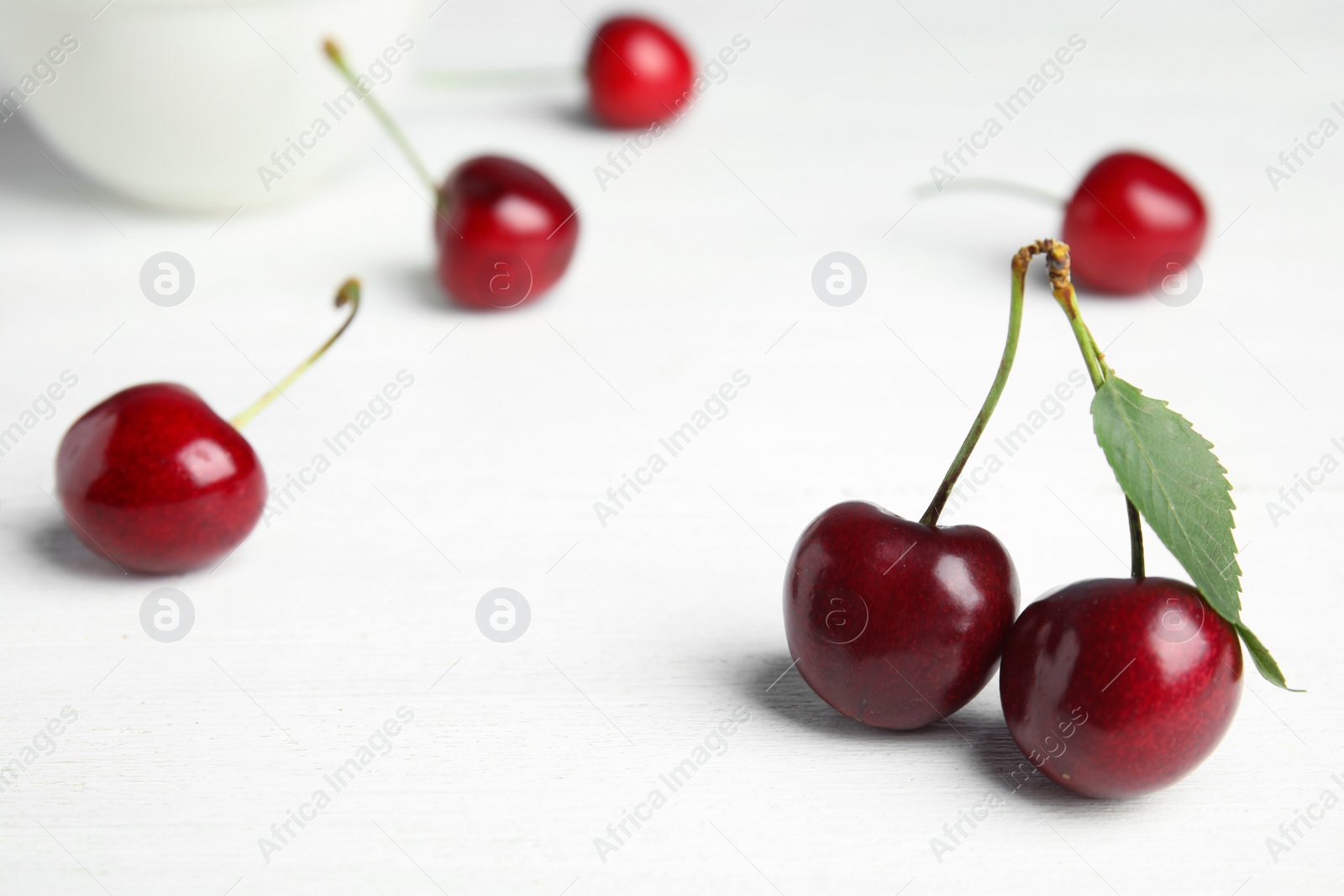 Photo of Ripe sweet cherries on white wooden table. Space for text