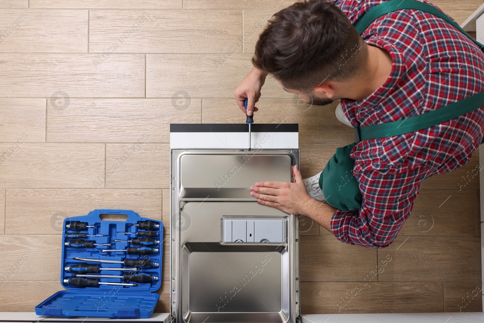 Photo of Serviceman repairing dishwasher's door with screwdriver indoors, top view