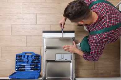 Serviceman repairing dishwasher's door with screwdriver indoors, top view