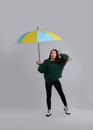 Photo of Emotional woman with umbrella caught in gust of wind on grey background