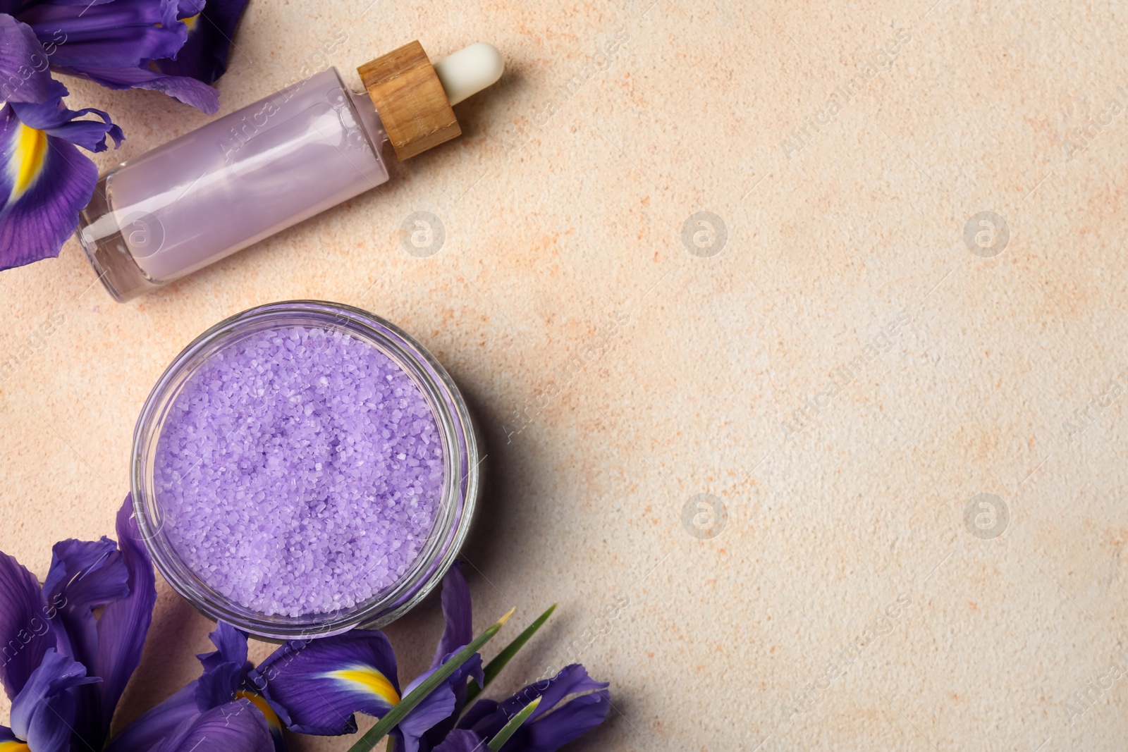 Photo of Aromatic sea salt, serum and flowers on beige textured table, flat lay. Space for text