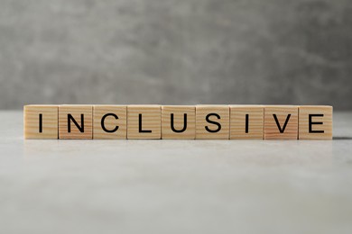 Photo of Wooden cubes with word Inclusive on grey table against blurred background