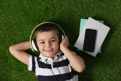 Photo of Cute little boy listening to audiobook on grass, top view