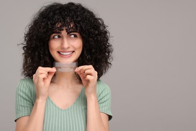 Young woman holding teeth whitening strips on grey background, space for text