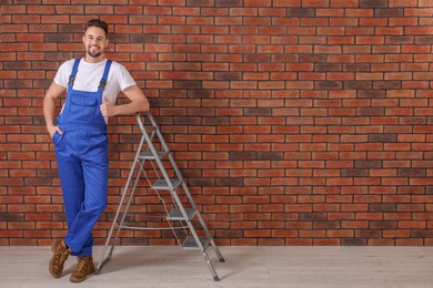 Happy worker showing thumb up near stepladder against brick wall, space for text
