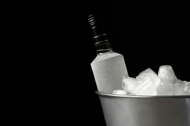 Photo of Bottle of vodka in metal bucket with ice on black background. Space for text