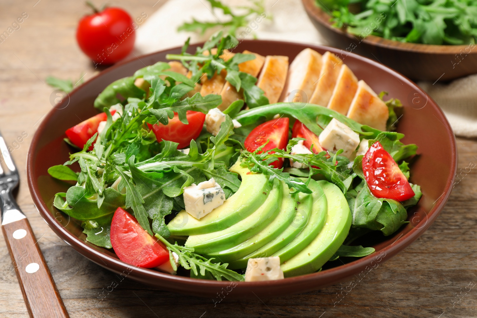 Photo of Delicious salad with chicken, arugula and avocado on wooden table, closeup