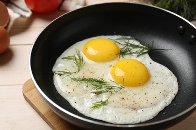 Frying pan with tasty cooked eggs, dill and other products on light wooden table, closeup