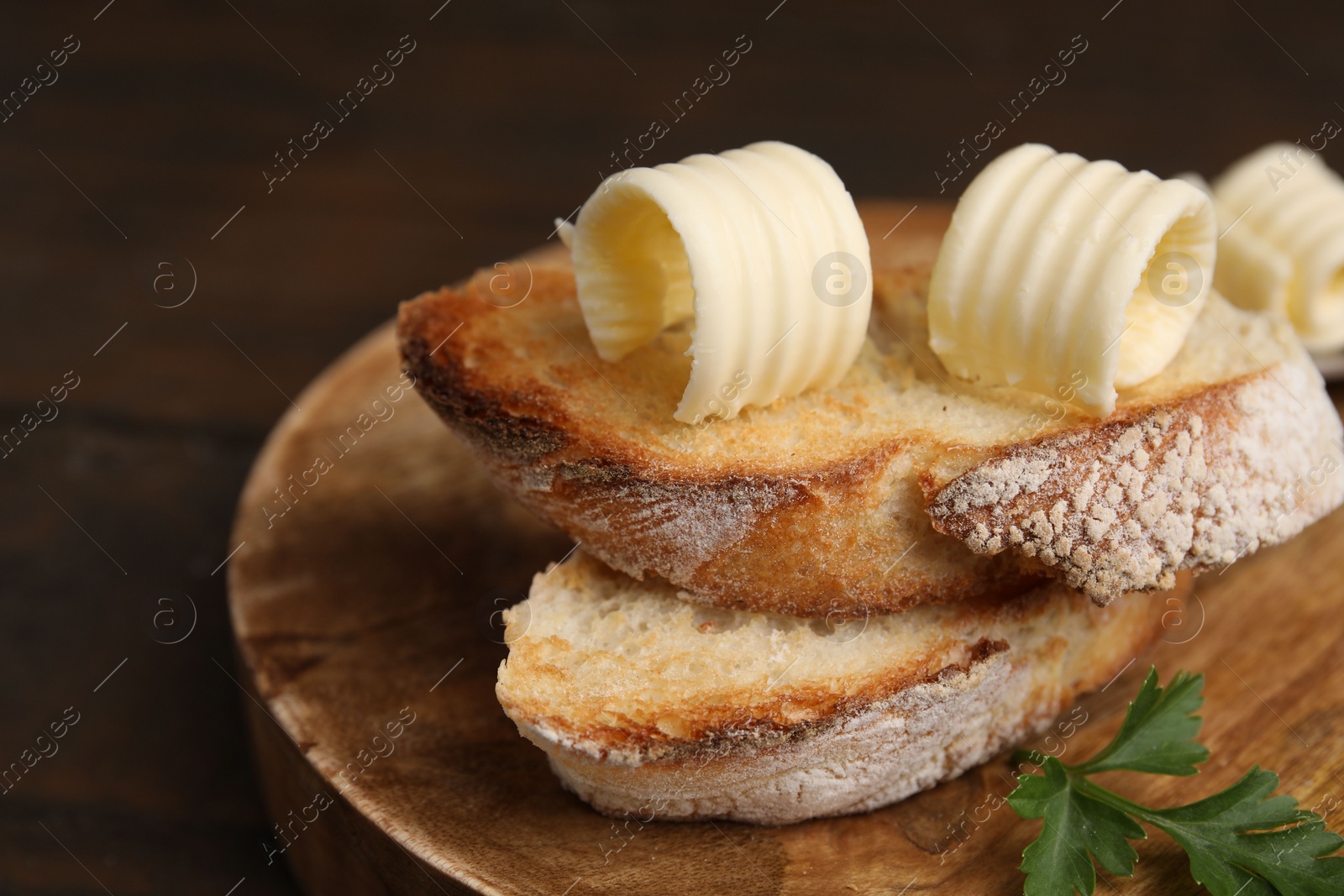 Photo of Tasty butter curls and slices of bread on wooden table, closeup