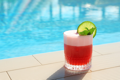 Photo of Glass of delicious cocktail near swimming pool, space for text. Refreshing drink